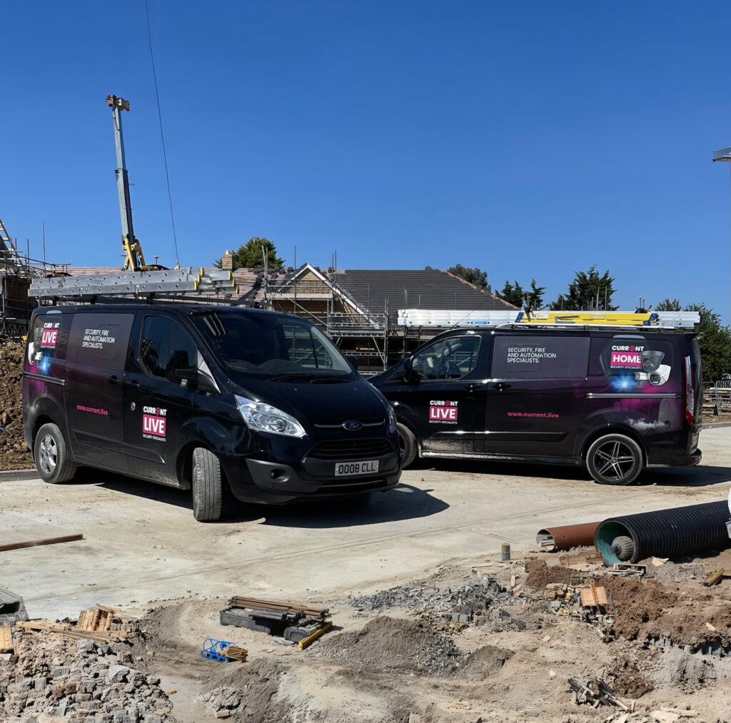 Two Currant Live branded commercial vans parked at a new housing development construction site.